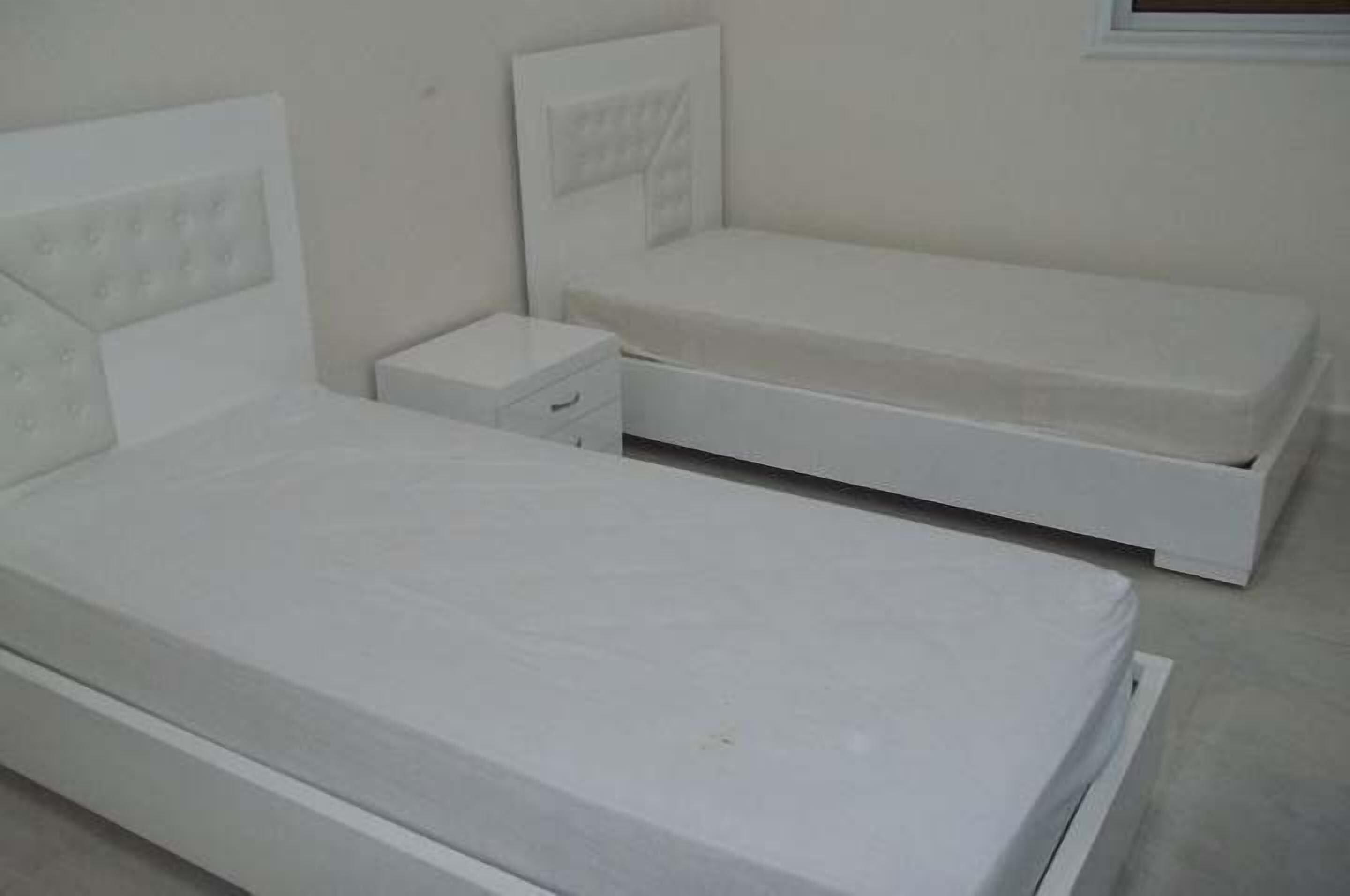A bedroom with two single beds, a nightstand, and a small drawer unit.