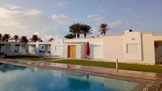 Un hotel moderno con piscina, palmeras y cielo despejado.