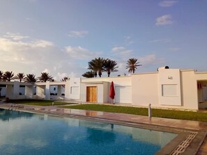 Un hôtel moderne doté d’une piscine, de palmiers et offrant une vue sur un ciel dégagé.