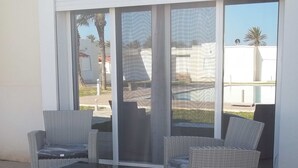 Un patio con mobiliario de mimbre, incluyendo dos sillas y una mesita, cerca de un ventanal corredero.