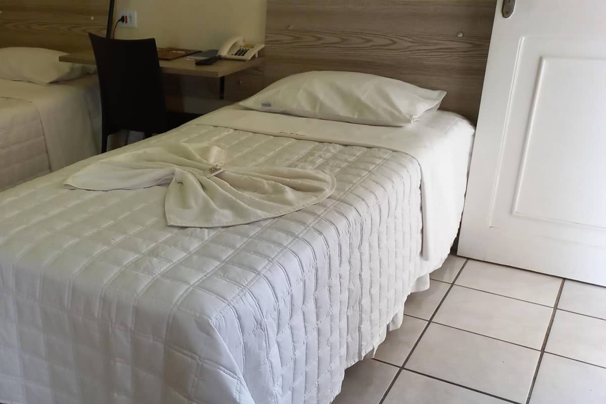Deux lits simples avec du linge de lit blanc et une serviette soigneusement pliée sur chacun.