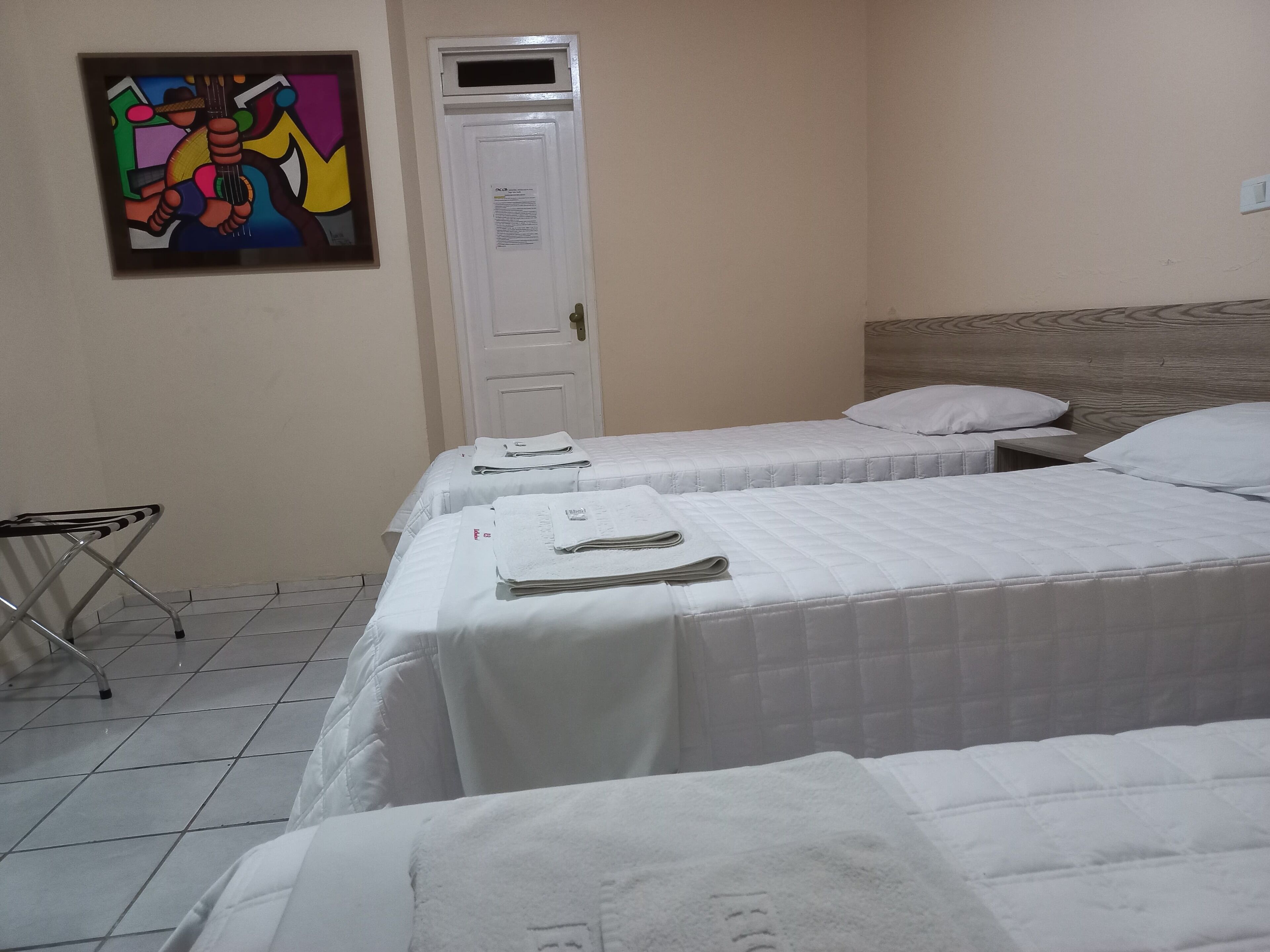 Quarto de hotel com duas camas, uma porta e um quadro abstrato colorido na parede.