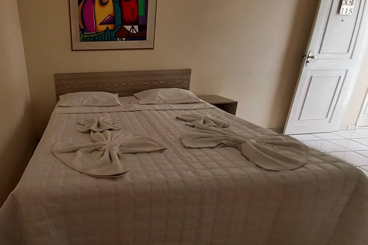 Un lit bien fait, avec une couvre-lit matelassé et des oreillers, une œuvre d’art encadrée au mur et une porte fermée en arrière-plan.