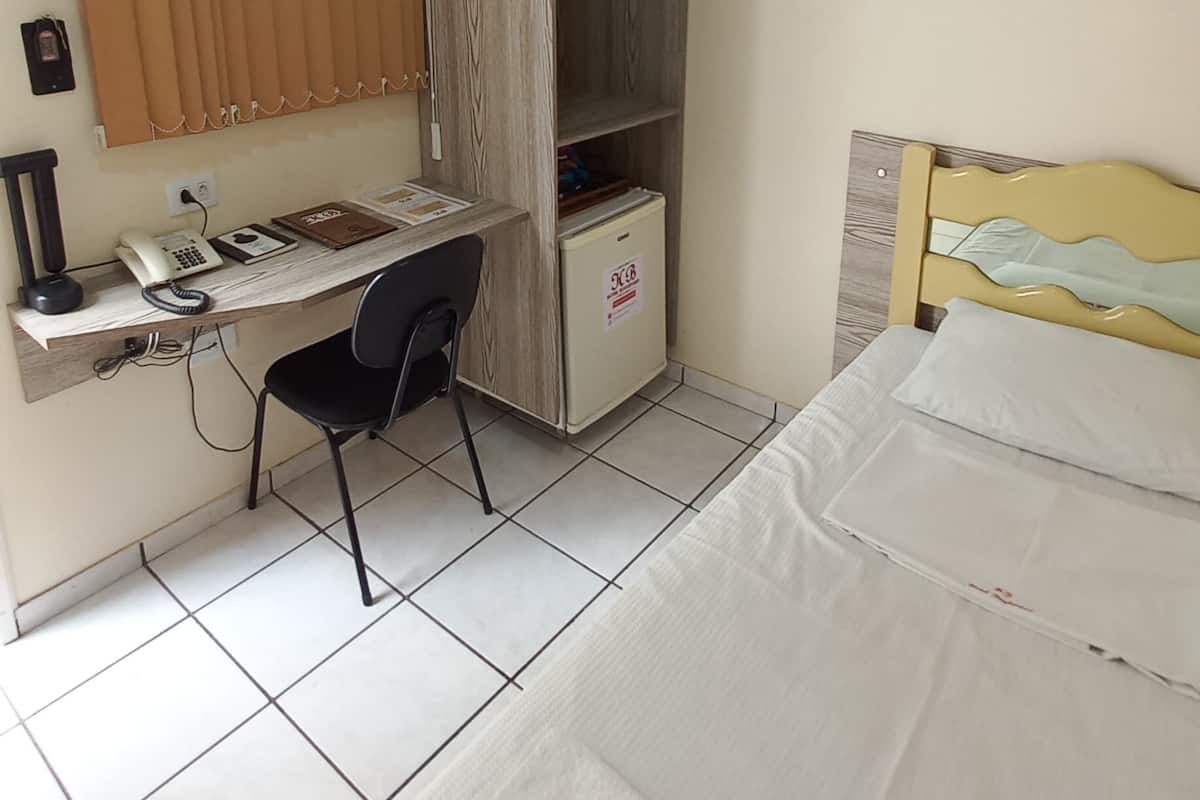 Une chambre à coucher avec un lit, un bureau et une chaise, une armoire et une fenêtre avec des rideaux.