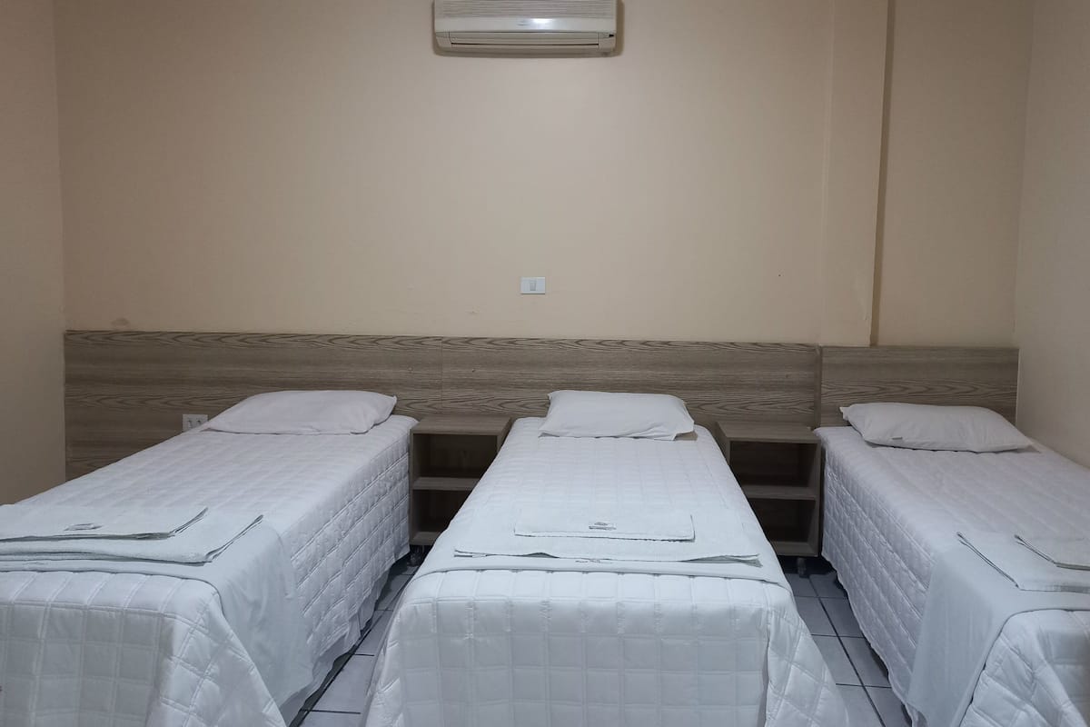 Une chambre avec trois lits simples, chacun doté d’une tête de lit en bois et de draps blancs.