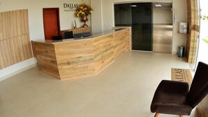 A reception desk with a wooden finish, a vase with yellow flowers, and a sign that reads "DALLAS". - Dallas Palace Hotel (Rio Paranaiba)