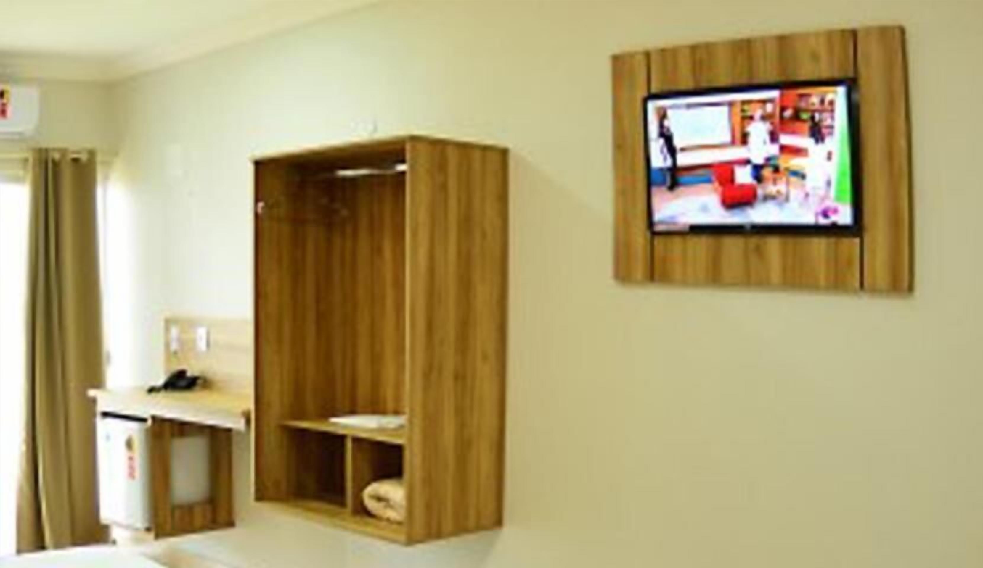 A hotel room with a wooden wardrobe, a desk, and a television mounted on the wall.