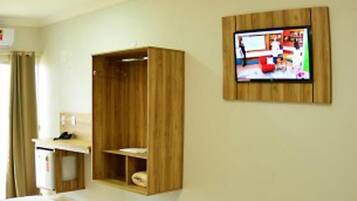 Una habitación de hotel con un armario de madera, un escritorio y un televisor montado en la pared.