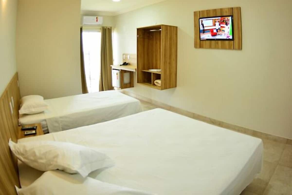 Ett hotellrum med två separata sängar, en TV som är monterad på väggen och ett träskåp.