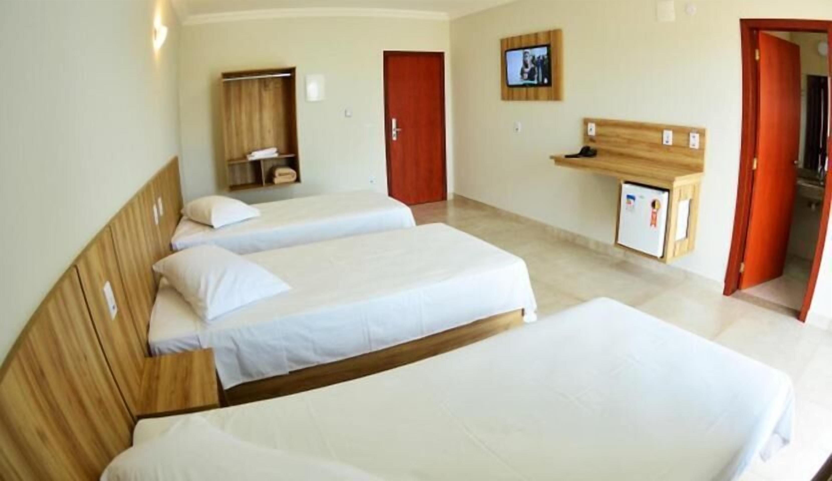 Une chambre d’hôtel avec deux lits, une tête de lit en bois, une télévision, un bureau avec une chaise et une armoire.