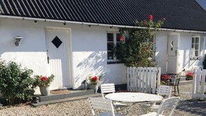 A white building with a black roof, a white door, and windows. There is a white fence, a gravel area with a white round table and four white chairs. - Ebogaard Bed and Breakfast (Hillerod)