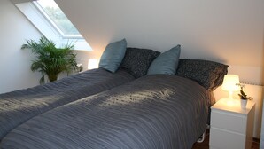 A bedroom with a skylight, a bed with grey bedding, two pillows, a bedside table with a lamp, and a small plant. - Ebogaard Bed and Breakfast (Hillerod)