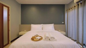 A hotel room with a bed, a bedside table, a tray with toiletries, and a window with curtains. - Schon (Chai Nat)