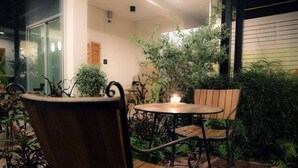 A patio area with a round table and two chairs, surrounded by potted plants and a small tree. - Schon (Chai Nat)