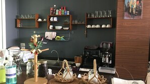 A kitchen with wooden shelves holding various kitchenware, a coffee machine, and a decorative item on the wall. - Schon (Chai Nat)