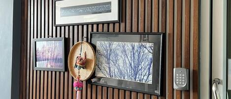 Pared con listones de madera verticales, un reloj, cuadros enmarcados, una cesta de mimbre, un teléfono y un revistero.
