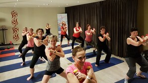 A group of people exercising with dumbbells in a room with blue mats on the floor, a curtain, and a wall with a decorative pattern. - Zen Your Life (Dilbeek)