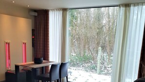 A modern bedroom with a large bed, a dining area, and a view of a snowy landscape through large windows. - Zen Your Life (Dilbeek)