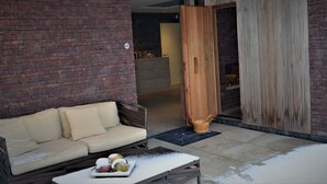 A cozy outdoor seating area with a sofa and a table, a wooden door, and a brick wall. - Zen Your Life (Dilbeek)