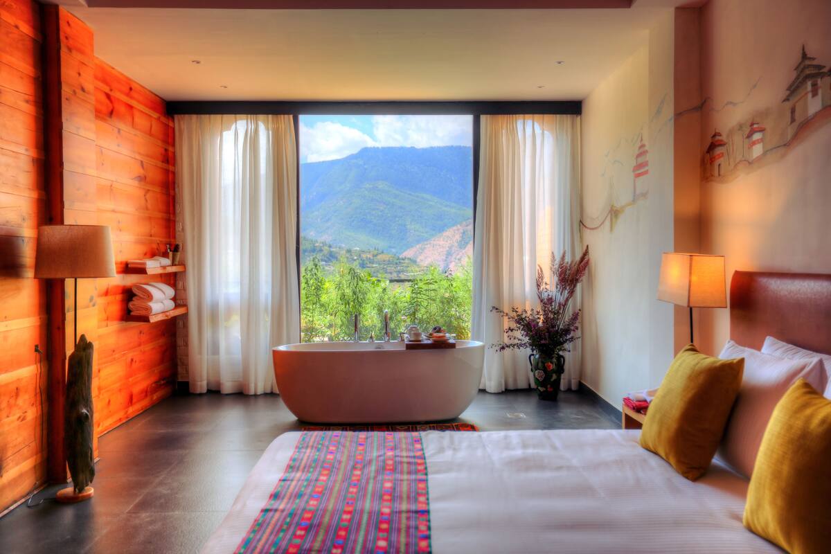 A hotel room with a large bed, a bathtub, and a view of mountains.
