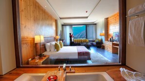A hotel room with a large bed, a wooden floor, a bathtub, and a view of a mountain. - Dewa Thimphu by Realm (Thimphu)