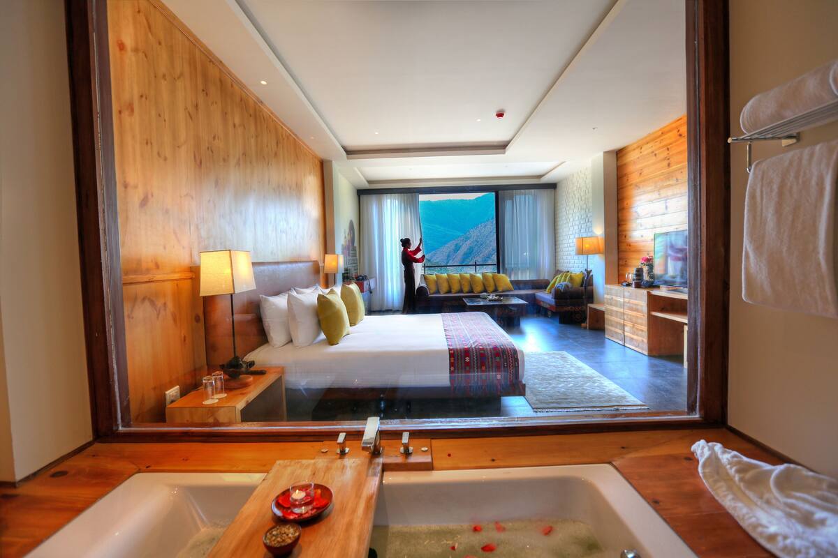 A hotel room with a large bed, a wooden floor, a bathtub, and a view of a mountain.