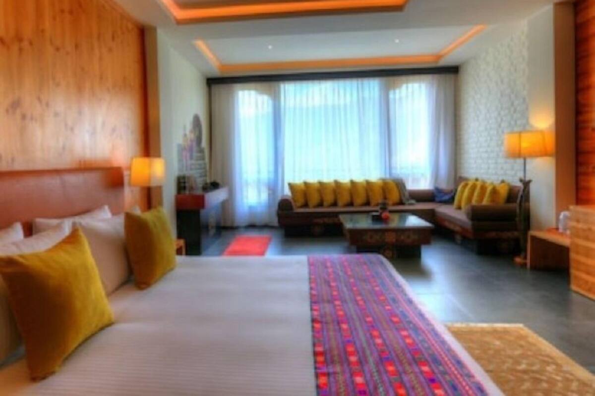 A hotel room with a large bed, a sofa, a coffee table, and a view of the city through large windows.