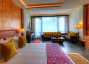 A hotel room with a large bed, a sofa, a coffee table, and a view of the city through large windows. - Dewa Thimphu by Realm (Thimphu)