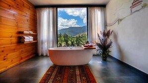 A modern bathroom with a freestanding bathtub, wooden paneling, a large window with a mountain view, and a decorative vase. - Dewa Thimphu by Realm (Thimphu)