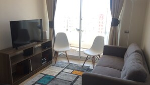 Ein Wohnzimmer mit Flachbildfernseher, zwei weißen Stühlen, einem grauen Sofa und einem gemusterten Teppich.