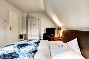 A hotel room with a bed, a chair, a nightstand, a lamp, and a door.