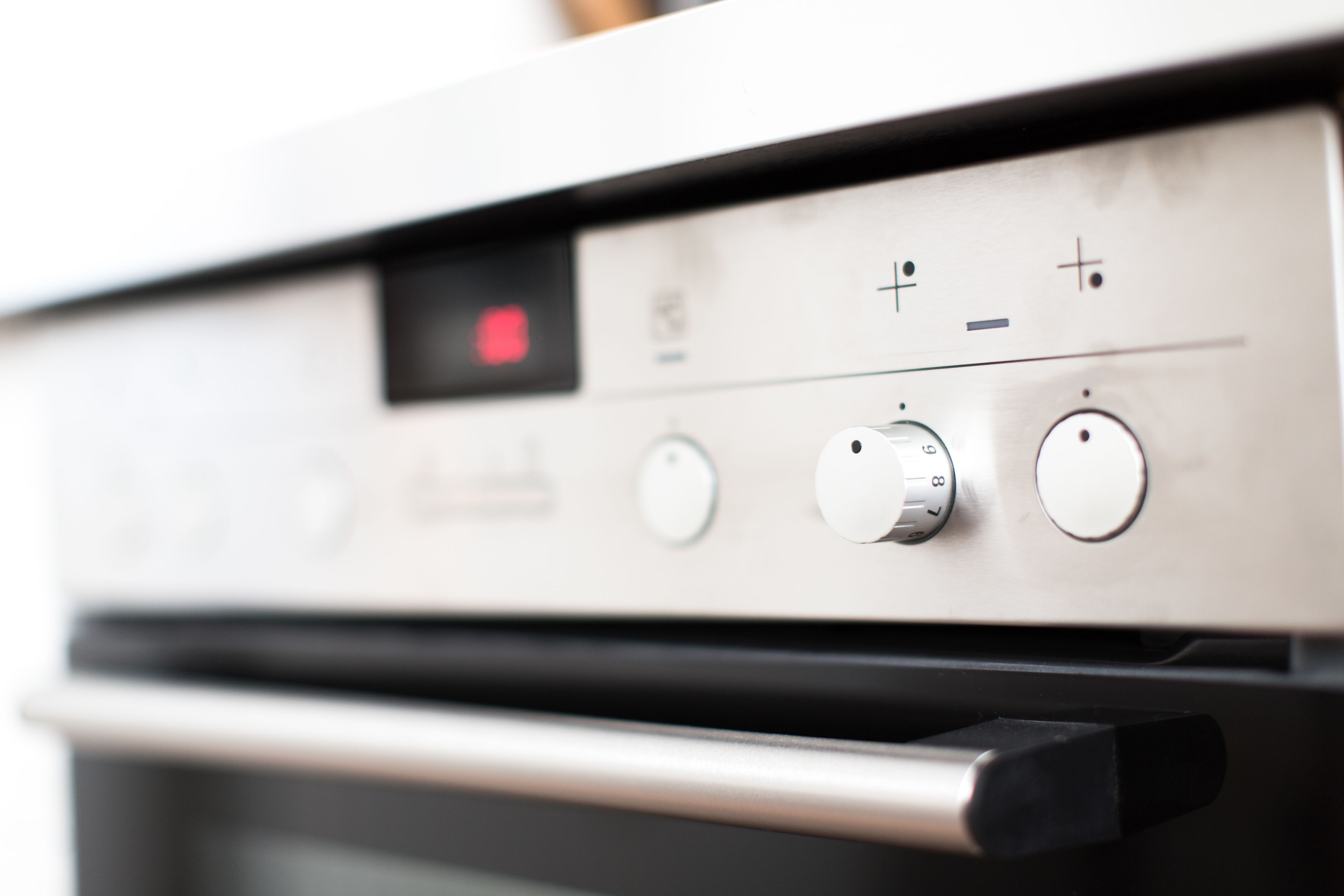 A close-up of an oven control panel with a digital display and several knobs.