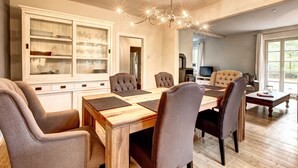 Un comedor con una mesa de madera y seis sillas, una araña y un aparador con puertas de cristal.
