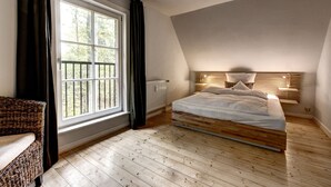 Un dormitorio con techo inclinado, una cama de madera, vistas a través de un ventanal grande y una silla de mimbre.