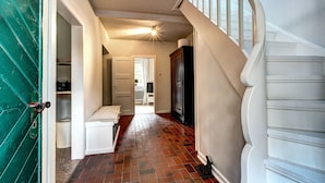 Un pasillo con piso de madera, un banco blanco y una escalera con barandales blancos.