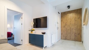 Un salon moderne avec un canapé, un téléviseur fixé au mur, une porte en bois et un radiateur blanc.
