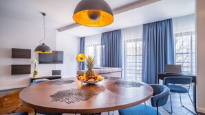 Un espace repas moderne avec une table ronde, des chaises bleues, un saladier de fruits et un luminaire suspendu.