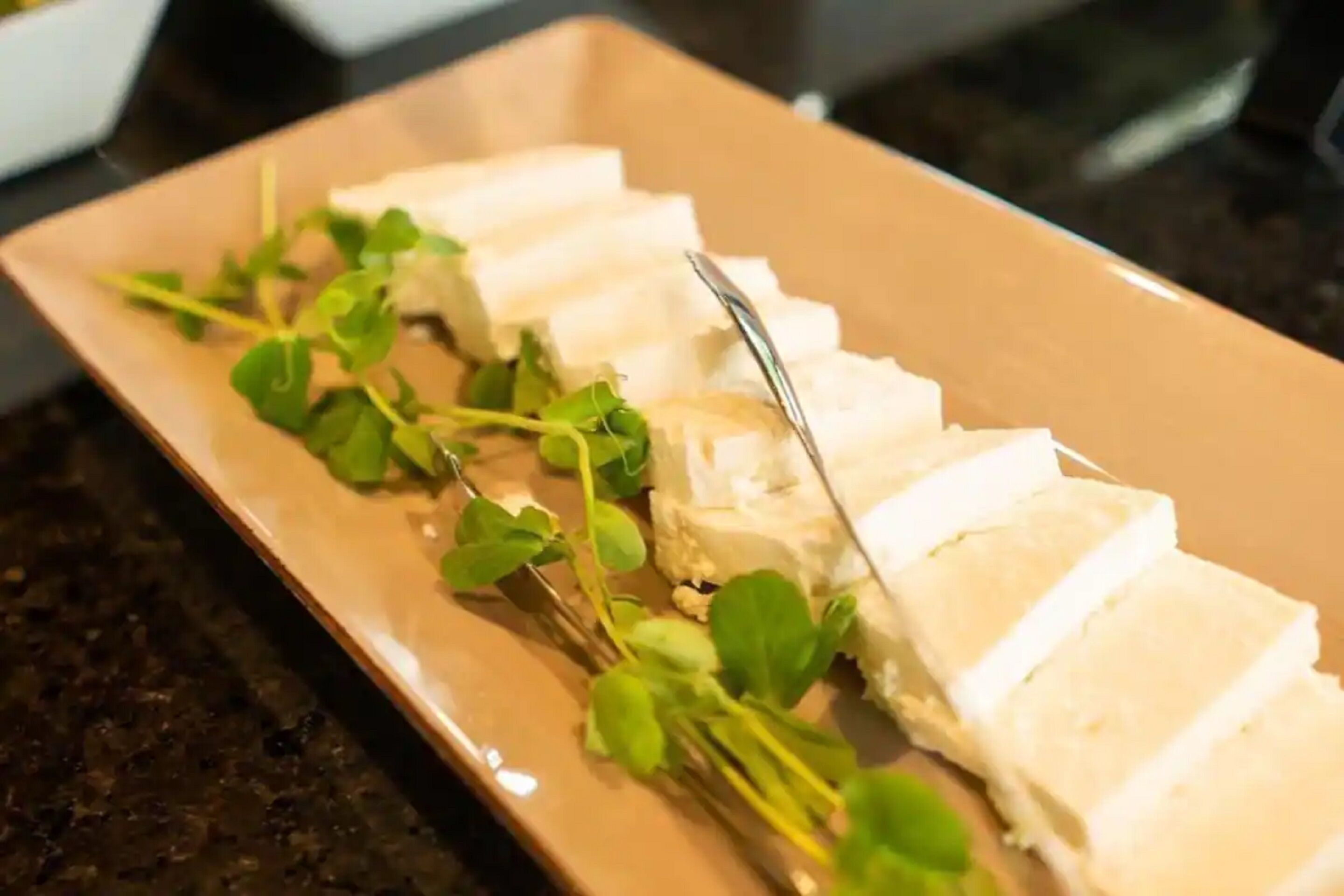 A rectangular plate with sliced white cheese and green leaves.