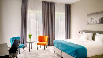 Una habitación de hotel con una cama grande, dos sillas, una mesita y una ventana con cortinas.