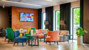 Un vestíbulo moderno con sillas coloridas, un televisor grande en la pared y ventanas amplias con cortinas.
