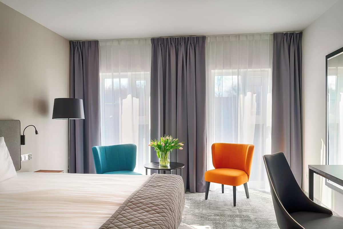 Ein Hotelzimmer mit einem Bett, zwei Stühlen, einem Tisch mit einer Vase und einer Lampe.
