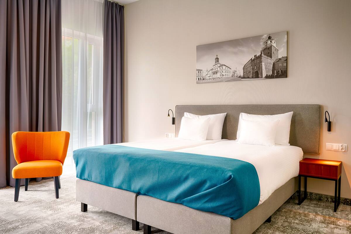 Une chambre d’hôtel avec un grand lit, une chaise, une table de chevet et une lampe fixée au mur.
