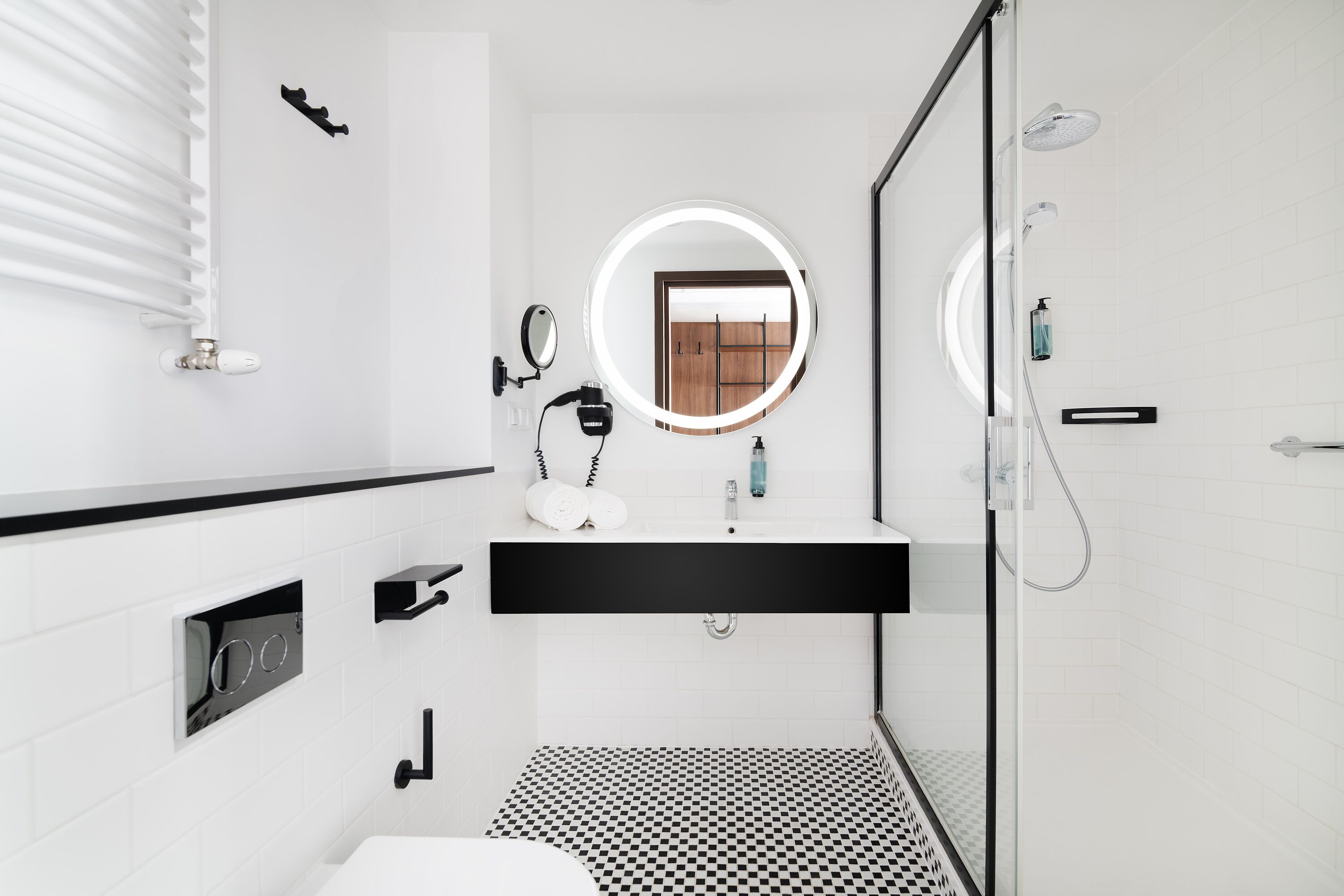 Un baño moderno con piso a cuadros blanco y negro, un espejo redondo, un cabezal de ducha manual y un inodoro.