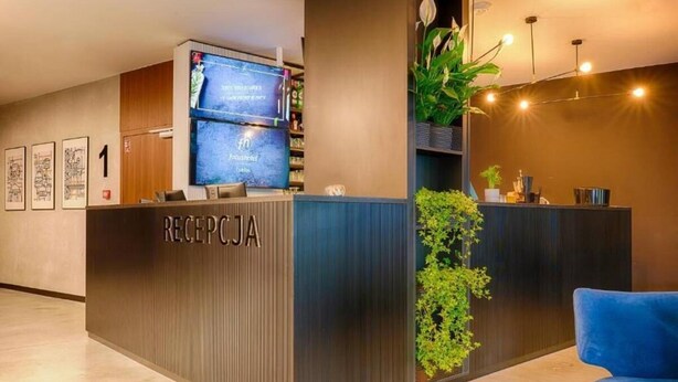 Un mostrador de recepción con una pantalla digital, una silla azul y una planta.