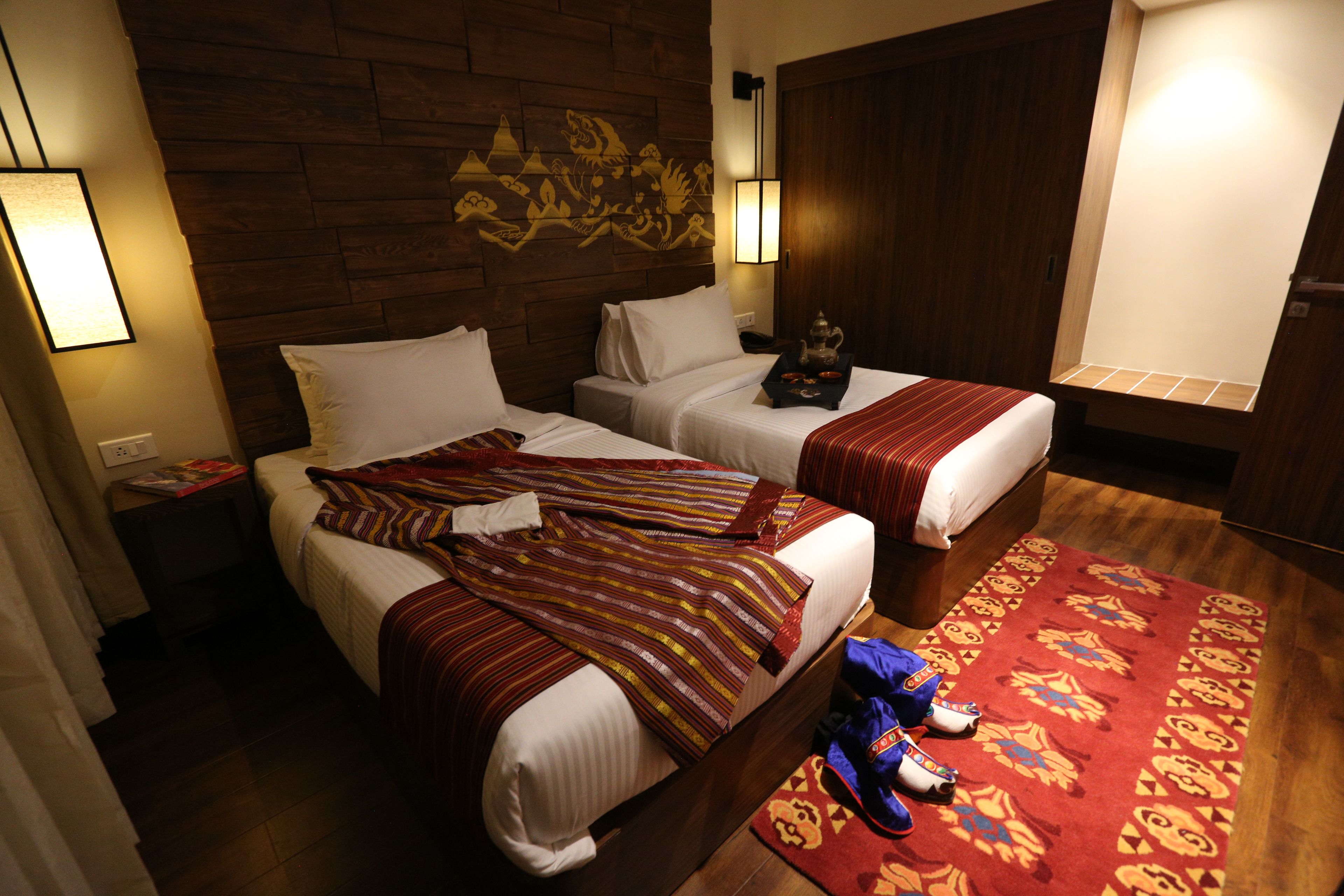 A hotel room with two beds, a wooden headboard, a decorative wall piece, and a patterned rug.