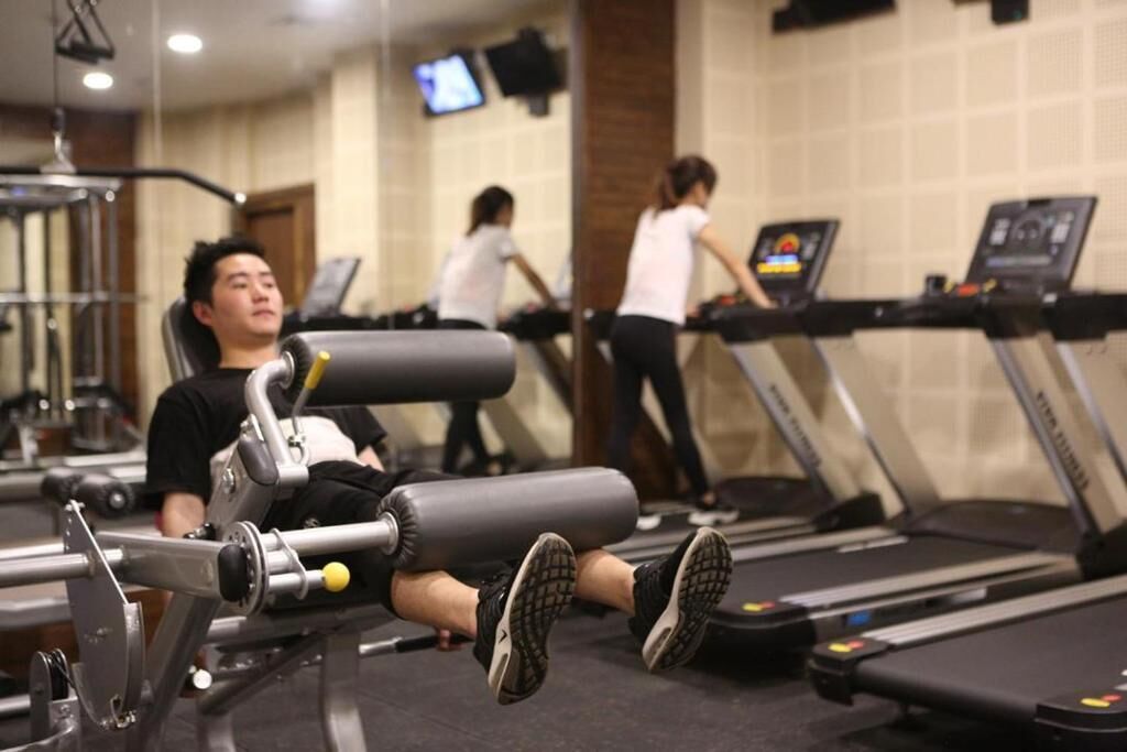 A gym with treadmills, weight machines, and a person using a leg press machine.