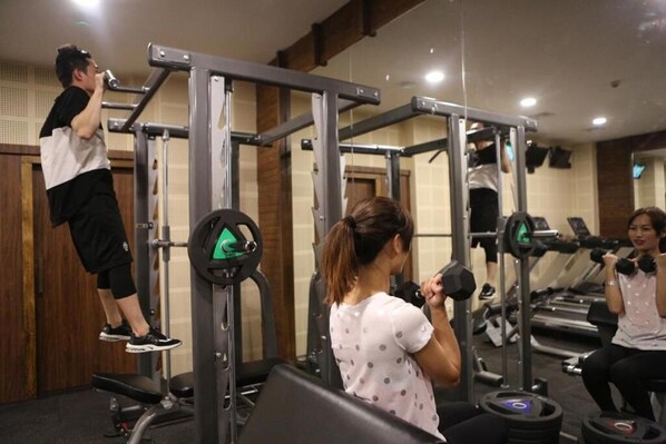 Un gimnasio con equipamiento de levantamiento de pesas, cintas de correr y un espejo.