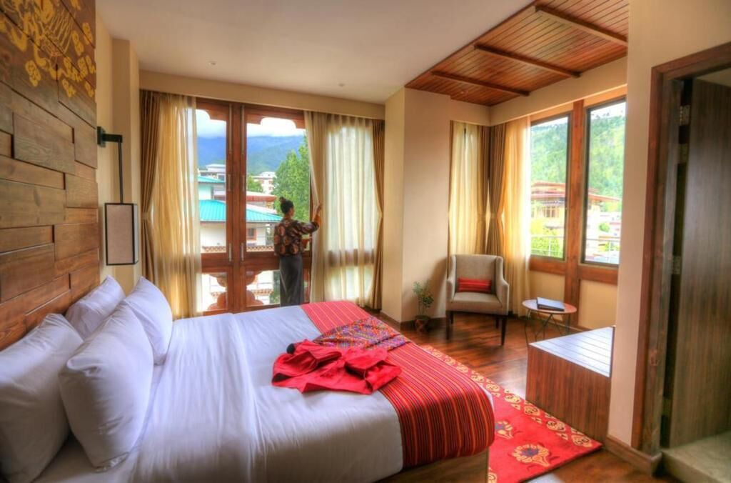Una camera d'albergo con un letto grande, una poltrona, un tavolino e vista sulle montagne.
