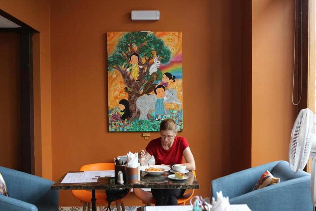 A room with a table set for a meal, a painting on the wall, and a fan.