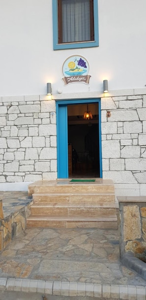 A building entrance with a stone facade, a blue door, and a sign above reading "Addayviz". - Adadayiz Otel (Bozcaada)